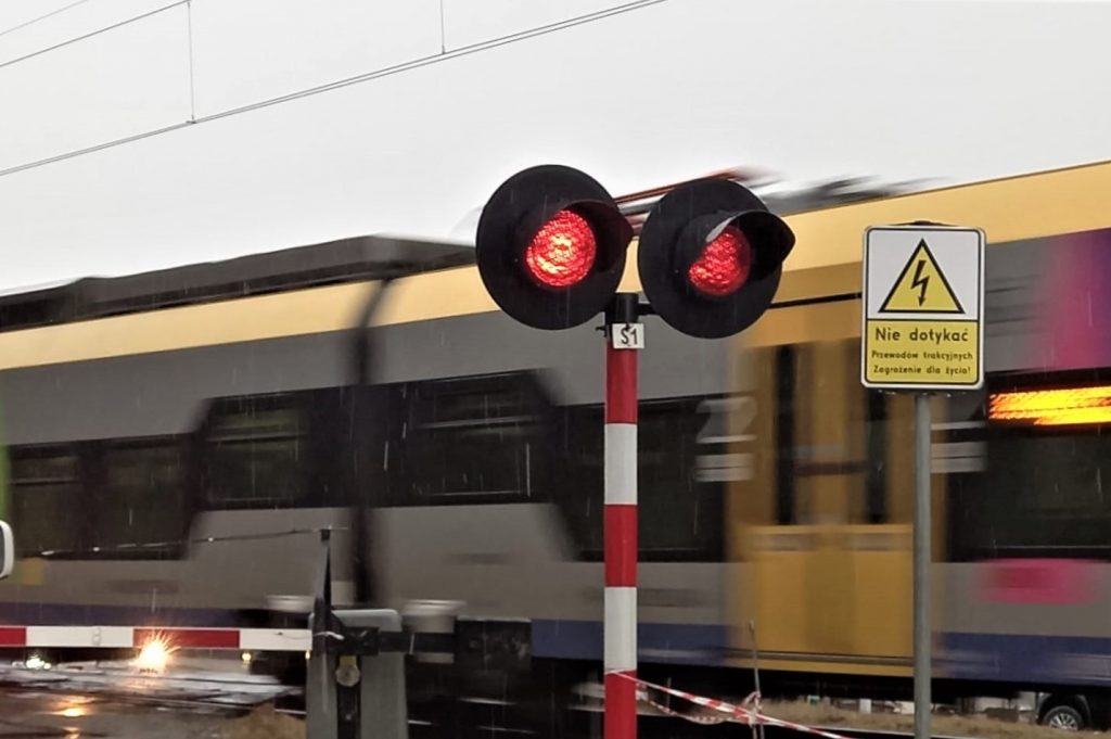 sygnalizator drogowy przejazdu kolejowego nadajacy swiatlo czerwone w tle przejezdzajacy pociag zdjecie ilustracyjne