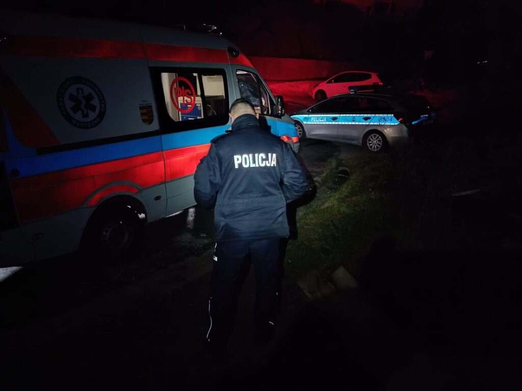 noc policjant stoi obok karetki dalej zaparkowany policyjny radiowoz