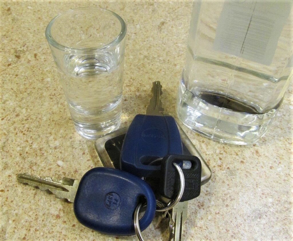 kluczyki do samochodu obok kieliszek i butelka z alkoholem