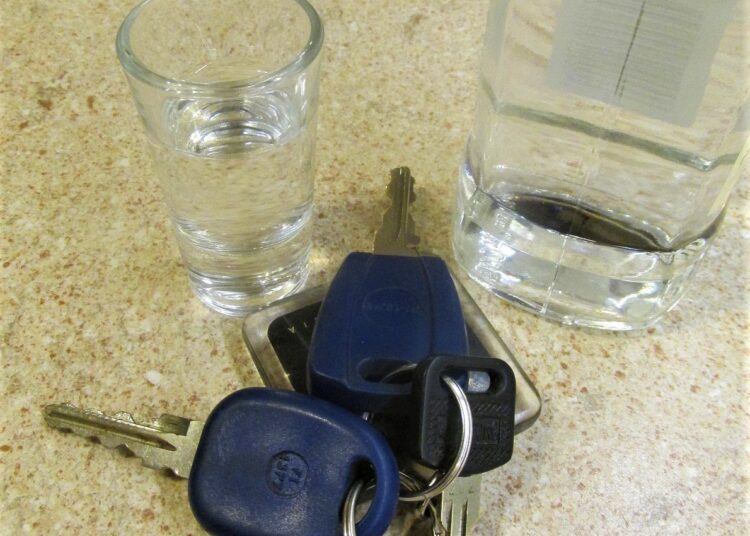kluczyki do samochodu obok kieliszek i butelka z alkoholem