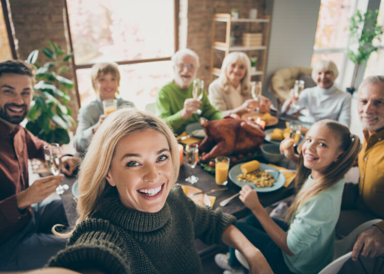 Photo of big family sit feast dishes table around roasted turkey multi-generation, relatives making group selfies raising wine glasses juice in living room indoors