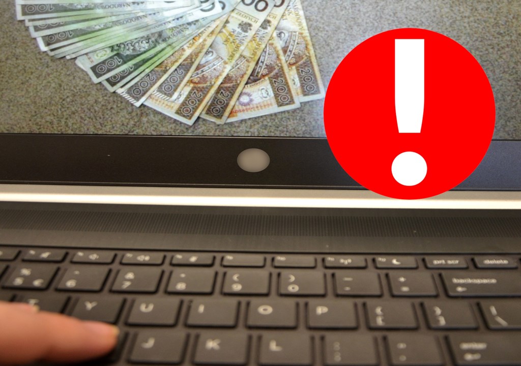 cyberoszustwa klawiatura laptopa na ekranie widoczne pieniadze obok czerwona znak z wykrzyknikiem