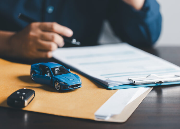 Businesswoman signing car insurance document or lease paper. Writing signature on contract or agreement. Buying or selling new or used vehicle. Car keys on table. Warranty or guarantee.