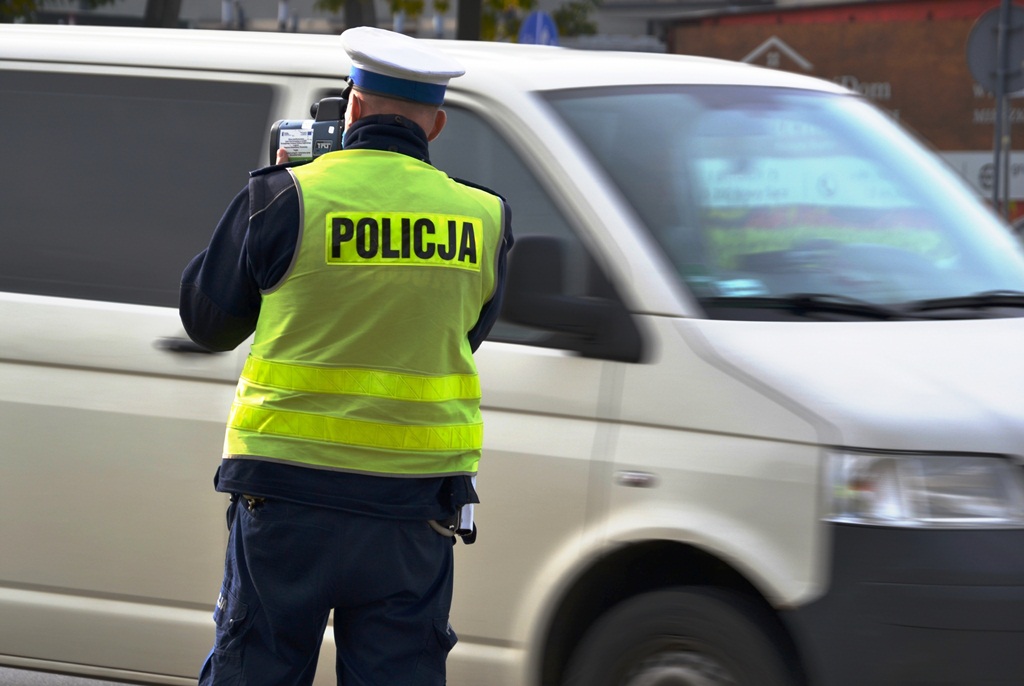 policjant z laserowym miernikiem predkosci w tle przejezdzajacy samochod