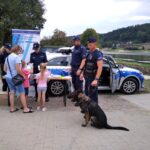 policjapolicjant z psem sluzbowym obok policyjny radiowoz i stoisko profilaktyczne Policji 1