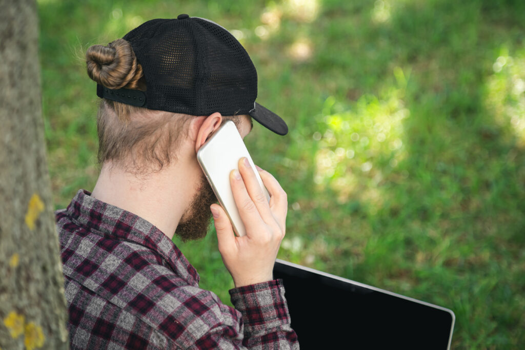 mezczyzna rozmawia na smartfonie siedzac na trawie z laptopem