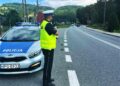 umundurowany policjant drogowki z laserowym miernikiem predkosci obok radiowoz w oddali jadace samochody