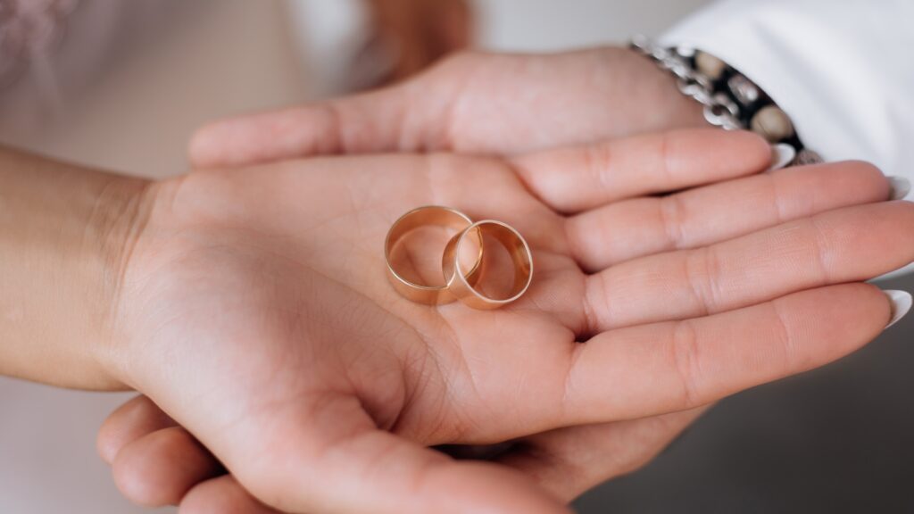 man woman hold two golden wedding rings their arms