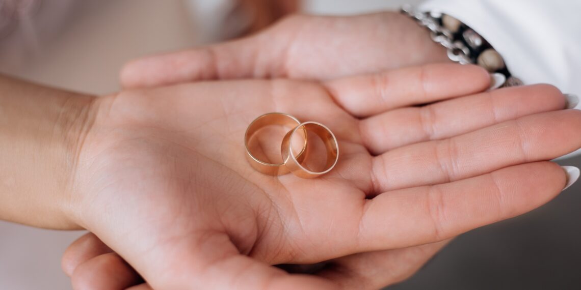 man woman hold two golden wedding rings their arms