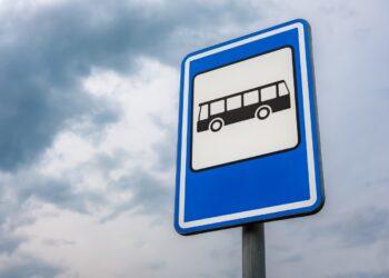 A low angle shot of a bus stop sign with a background of blue cloudy sky